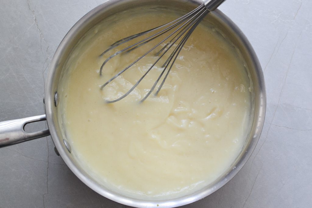 cooked Gluten free pudding in a saucepan with a whisk
