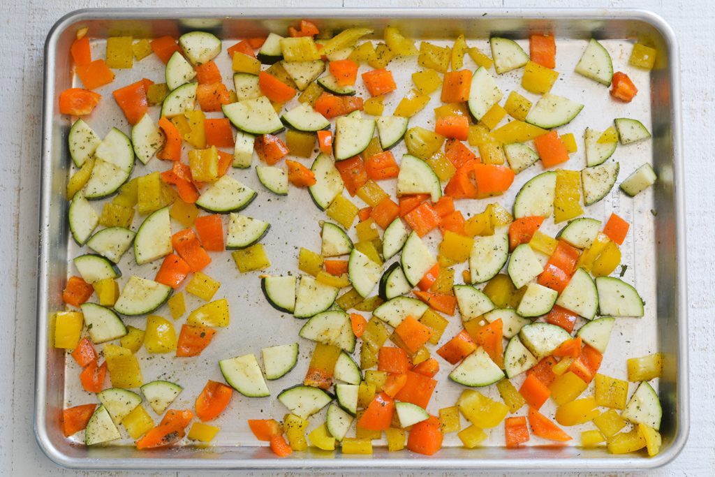 zucchini and peppers on a sheet pan with seasoning